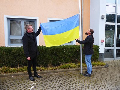 Der Bürgermeister und der Hauptamtsleiter hissen die ukrainische Flagge.