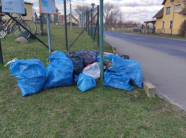 Gesammelter Müll in Säcken, die vor dem Zaun des Areals der Bockwindmühle und der Bürger- und Tourismusinformation liegen.